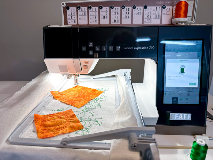  A white and black embroidery machine with an endless hoop attached, filled with cream woven fabric, embroidered with the Endless Pumpkin design after appliqueing the pumpkins (in orange fabric).