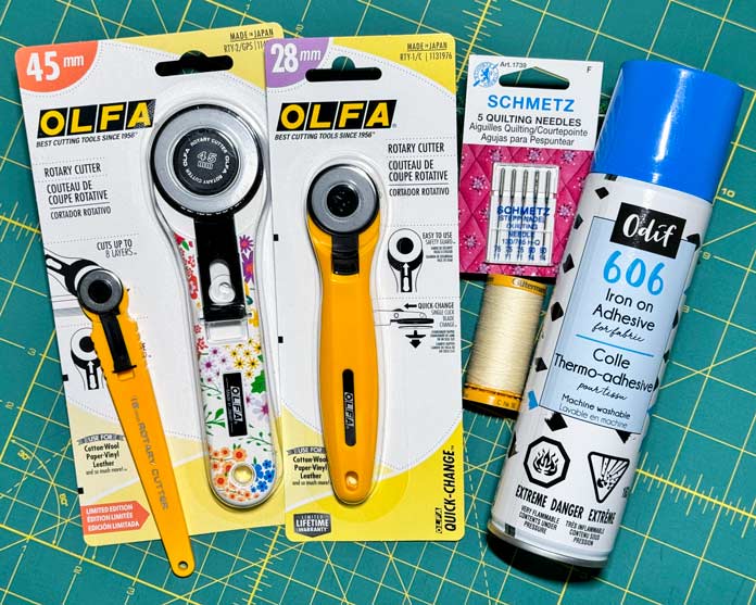 Three OLFA rotary cutters and 18mm, 45mm and a 28; A spool of Gütermann thread, a Pack of SCHMETZ quilting needles and a can of Odif 606 iron-on adhesive spray. 