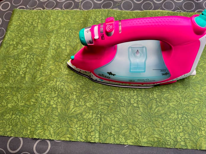An Oliso PRO TG1600 Pro Plus Smart Iron is used to press a piece of green fabric.