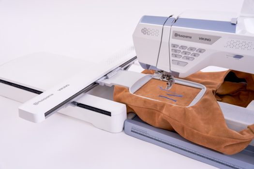 A white and blue sewing machine with brown fabric in an embroidery hoop