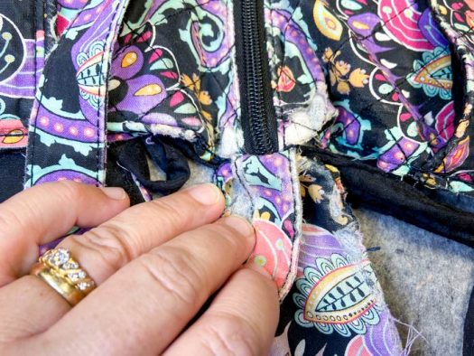 A hand holds the strap of a multicolored purse to show how it has been sewn to the end of the zipper.
