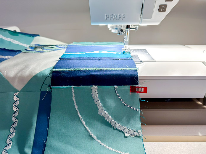 Sections of teal, blue green fabrics, enhanced with decorative stitching, pieced into a decorative table center quilt.
