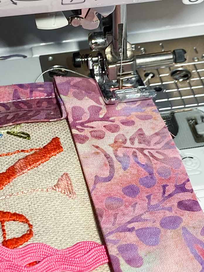 Pink floral batik binding is sewn to one corner of a piece of embroidered fabric.