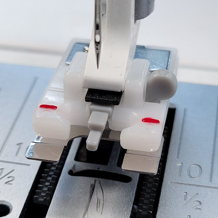 A presser foot on a sewing machine for sewing buttons on; Husqvarna Viking Designer Ruby 90, Button Foot with Placement Tool