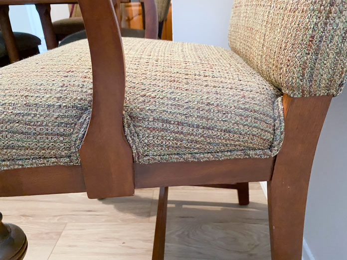 A wooden chair with a light brown fabric seat and double welting where the upholstery meets the wood