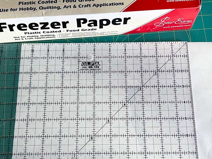 An 8½” x 11” of freezer paper cut with a quilting ruler on a cutting mat; OLFA 12.5″ Square Frosted Acrylic Ruler, Sew Easy Freezer Paper for Quilting and Applique - 12.1m x 38.1cm (13.2yd x 15″)