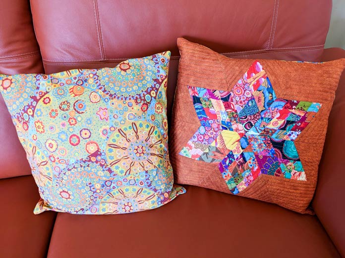 Two pillows on an orange leather couch; the first shows the back of the pillow, the second shows the front of the 6-point start pillow with echo quilting