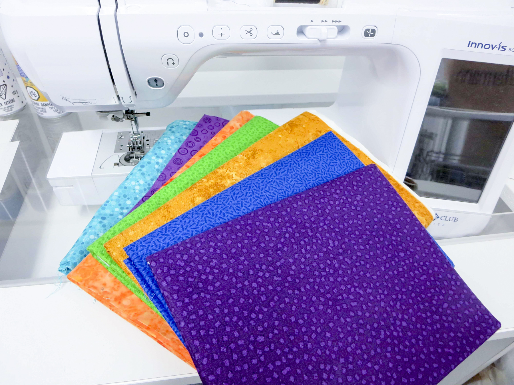 Purple, blue, orange, green, and turquoise cotton fabrics for the wall quilt lay on a white sewing machine.