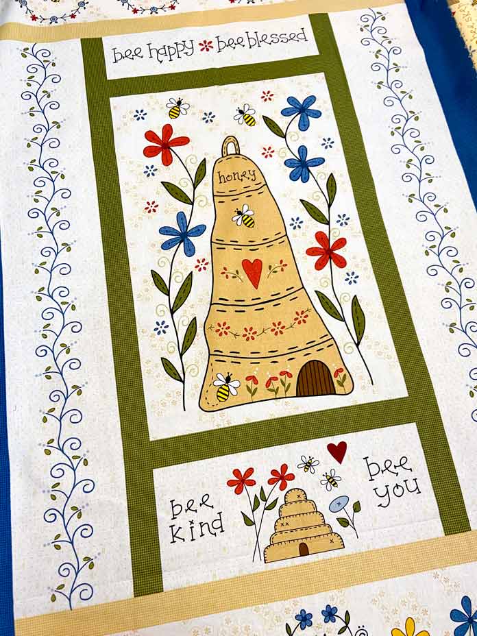 A cream fabric panel with bees, bee skeps, flowers and words. 