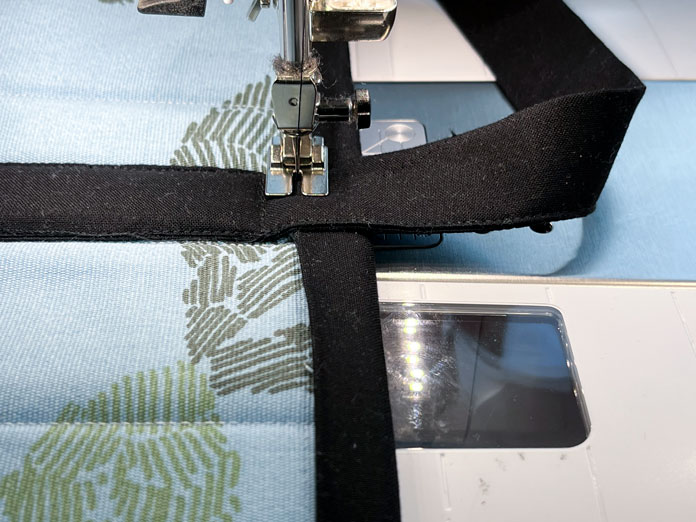 Sewing down the handles of the bag at the same time as sewing down the binding to the upper edge of the bag.