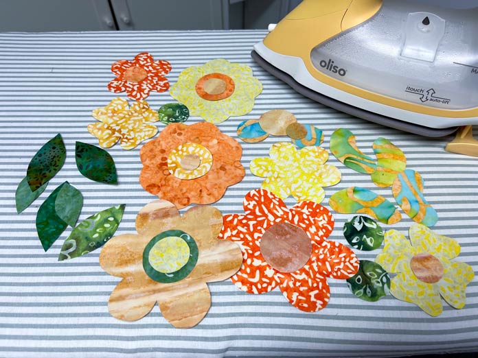 Fabric flowers in oranges and yellows and green leaves next to a yellow iron; Oliso Pro TG1600 Pro Plus Smart Iron