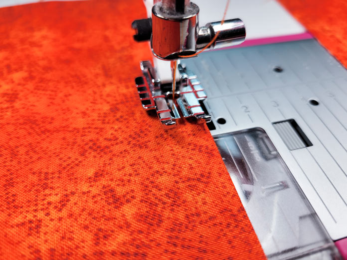 An orange piece of fabric under a metal presser foot; Husqvarna Viking DESIGNER EPIC 2