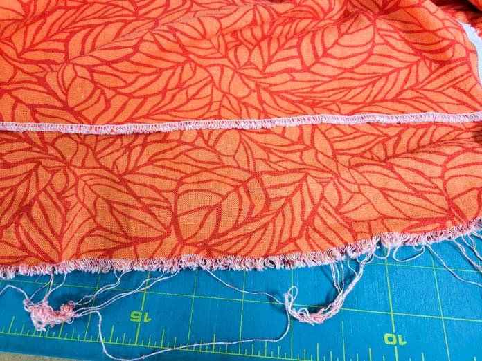Orange fabric with a stitched edge and an edge with frayed threads
