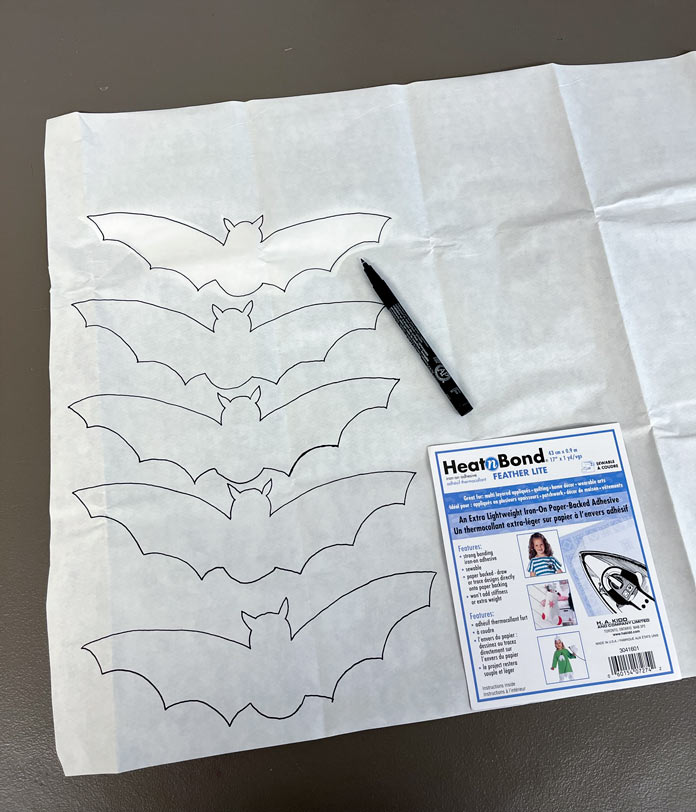 Preparing the bat appliques by tracing the bat design onto the paper side of the fabric adhesive with a marker
