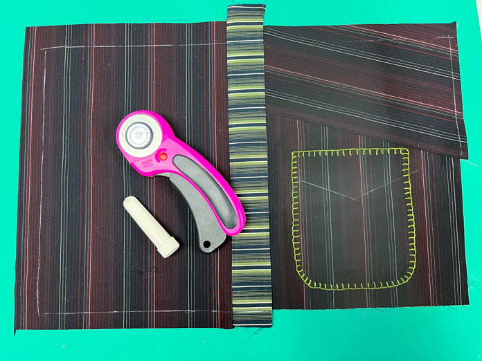 Pieced placemat with chalk line is shown with rotary cutter and chalk laying on top; OMNIGRIP Ruler 8½" x 8½", OLFA 45 mm Ergonomic Rotary Cutter, OLFA Endurance Rotary Blades, Sulky Tear-Easy stabilizer, Odif 505 Adhesive Fabric Spray, OLISO PRO TG1600 Pro Plus Smart Iron, Mary Ellen’s Best Press, Best Press Spray and Misting Bottle