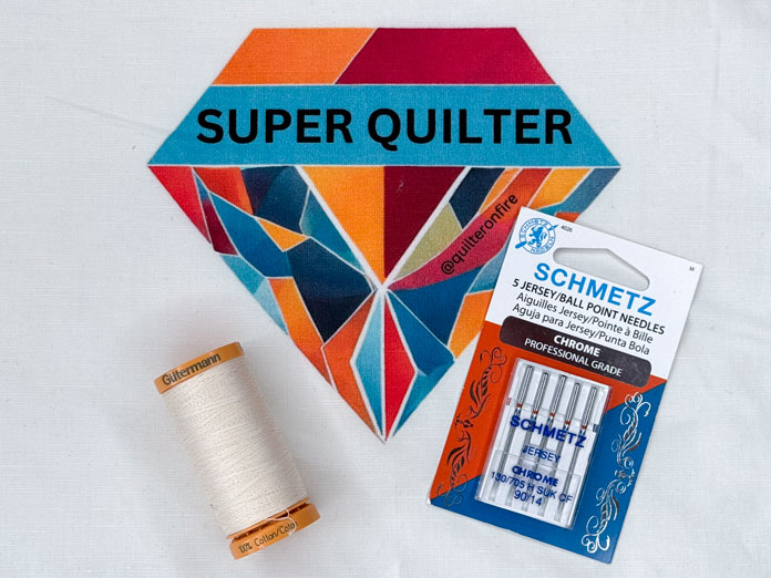 A GÜTERMANN Cotton 50wt thread and SCHMETZ Chrome Jersey needles on a T-shirt block that has the words Super Quilter.