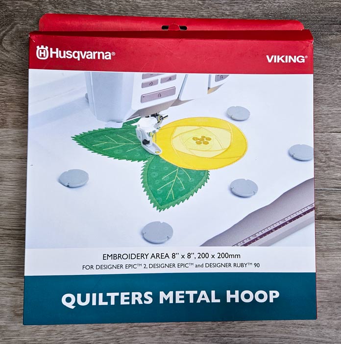 A red and white box with a green and yellow floral design; Husqvarna VIKING Quilters Metal Embroidery Hoop 200mm by 200mm