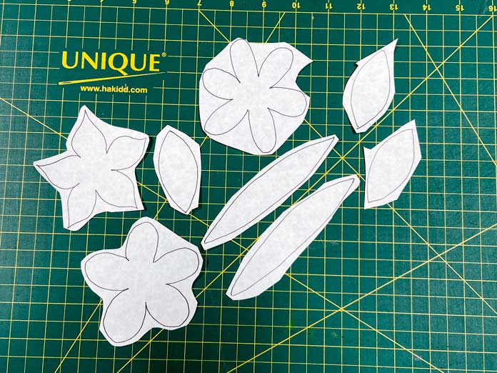 Three flower shapes and six-leaf shapes drawn onto the paper side of the HeatnBond EZ Print Feather Lite have been cut out and sit on a green cutting mat.