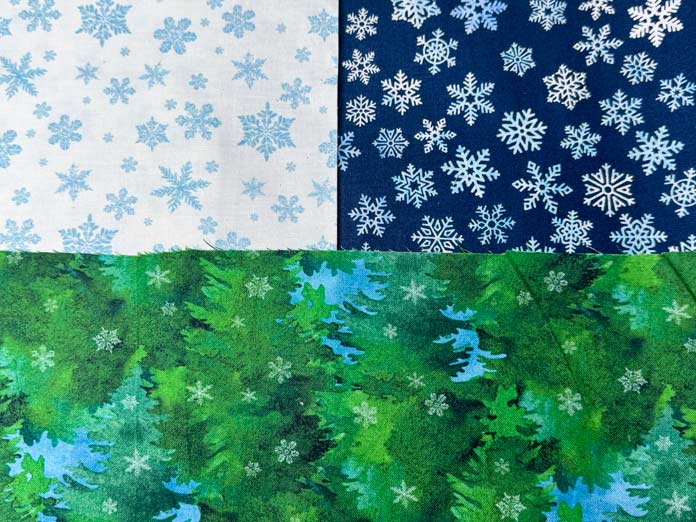 The fabric selection for the quilt; A white and dark blue snowflake fabric with a green and light blue tree fabric.