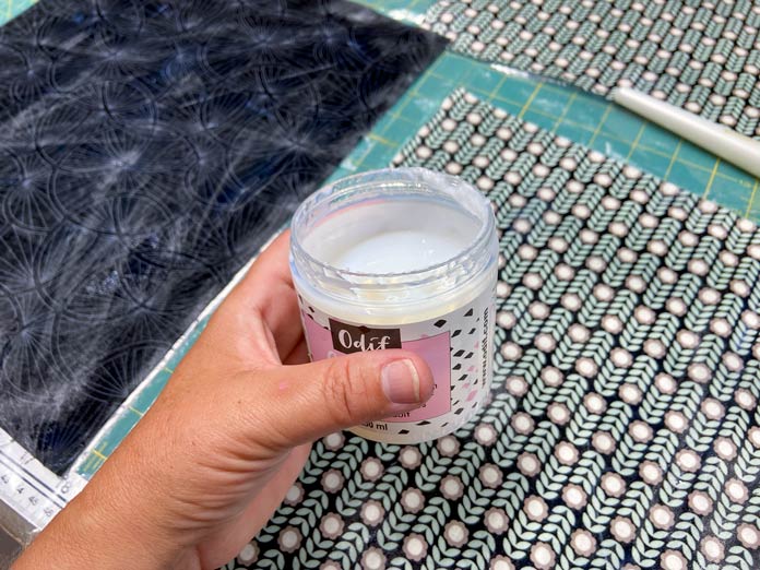 A hand holds a half-full jar of Odfi OdiCoat over top of treated fabrics.