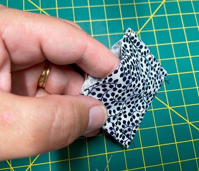 A hand holds a small pouch made of black and white fabric. A green cutting mat is in the background.