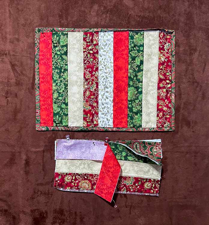 A strip pieced placemat using Christmas fabrics and partially bound and below it is showing the layers put together in a quilt-as-you-go technique, 4 layers of cotton and 2 layers of quilt bat; PFAFF admire air 7000 serger 