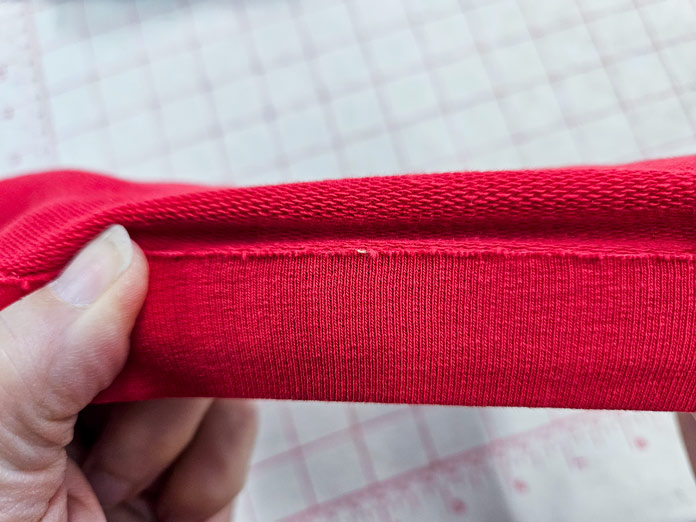 The hem of a red knit fabric stretched; HeatnBond, fusible web, sewing, applique, quilting, hemming, fabric adhesive, SoftStretch, Lite, Featherlite, Ultra, sewing tips, crafting, fabric experiments