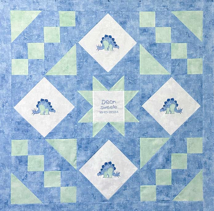 Blue and Green pieced quilt with 4 blue and green appliqued dinosaurs on white blocks, NSWE positions and a center embroidered white block, with blue embroidered words; PFAFF creative expect 350, sewing machine reviews, mySewnet Quilting Software, mini quilt finishing, beginner quilting tips, quilt binding guide, machine quilting techniques, organic quilting, embroidery quilt labels, diy quilt projects, free motion quilting, free quilting project, free quilting patterns, baby quilt, free quilting tutorials