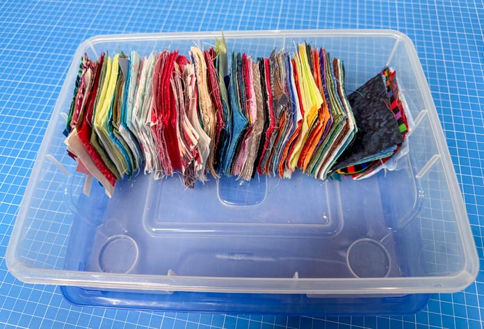 A plastic bin containing 3” x 3” squares of multiple colors.