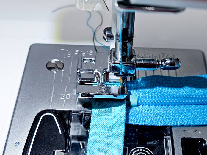 A metal zipper foot on a sewing machine