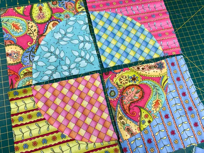 Four brightly coloured Drunkard’s Path blocks lay in a four-patch arrangement on top of a green cutting mat.