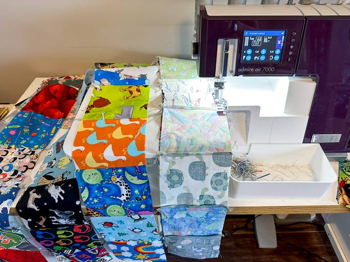 A white and burgundy serger stitching rows of unique kid prints in 5” squares together to make a I Spy quilt