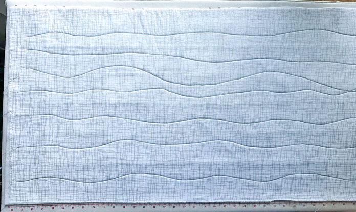 A white fabric with silver flecks, with gray wavy stitch lines going from top to bottom.
