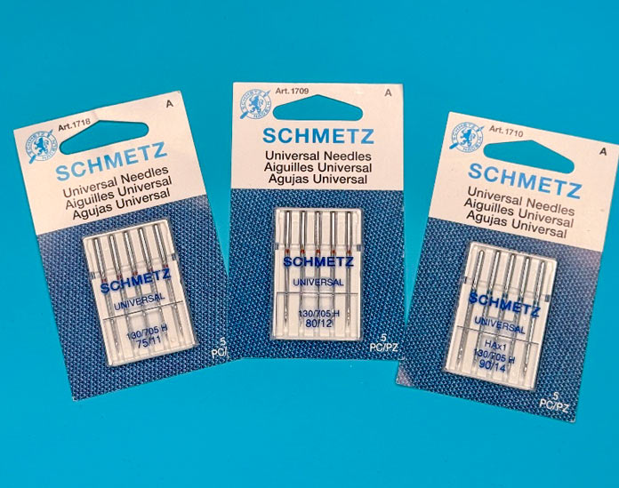 Multiple packages of different SCHMETZ Universal sewing machine needles and sizes.