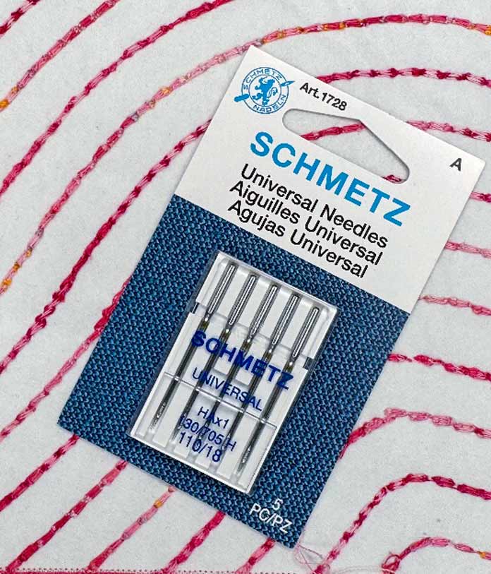 A package of SCHMETZ 100/18 Universal sewing machine needles on a piece of quilted fabric.