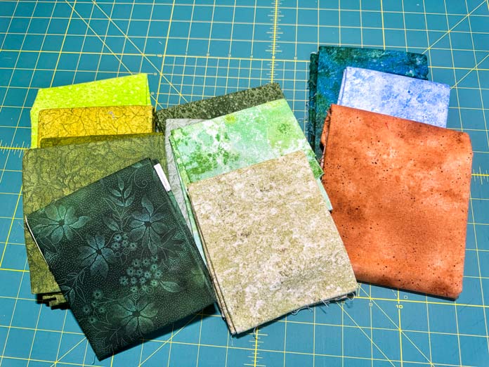 A selection of green fabrics with a blue and rust colored fabric.