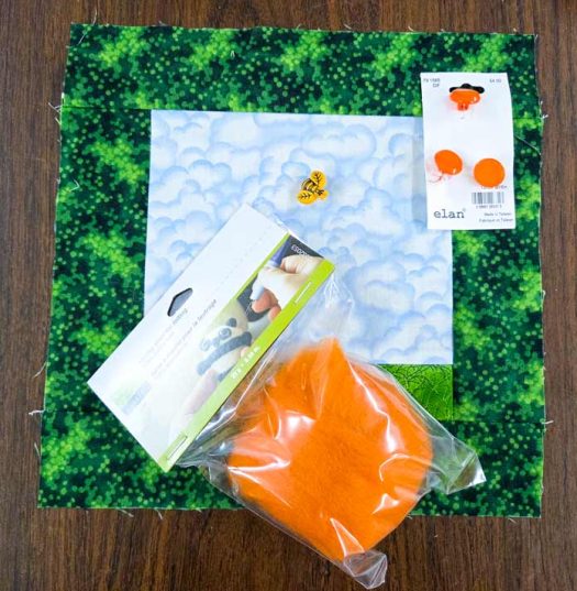 A green and blue square of fabric, orange roving, orange buttons, a bee button; : UNIQUE Craft roving, Elan Orange Shank Buttons, Dress it Up Large Bee buttons