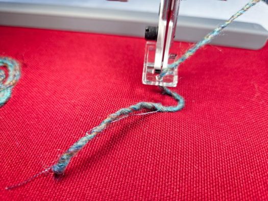 Yarn in an embroidery machine presser foot on red fabric
