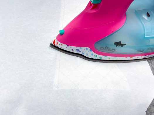 A pink iron presses a piece of freezer paper that has a purse section underneath.