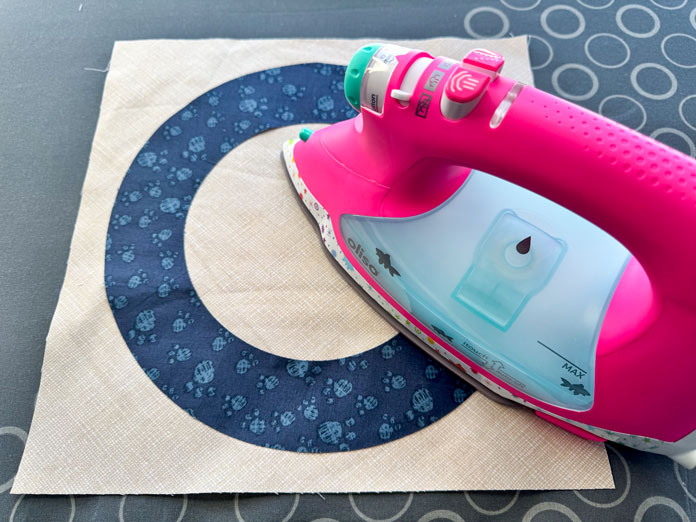 An oliso iron pressing a fabric donut on a fabric square.