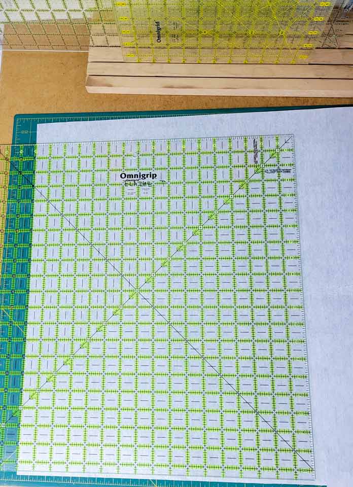 A large quilting ruler on a piece of white stabilizer; Husqvarna Viking Designer Ruby 90 sewing and embroidery machine, Inspira Fusible Fleece, Omnigrip 20½" square ruler, Singer 20 Steam Garment Press