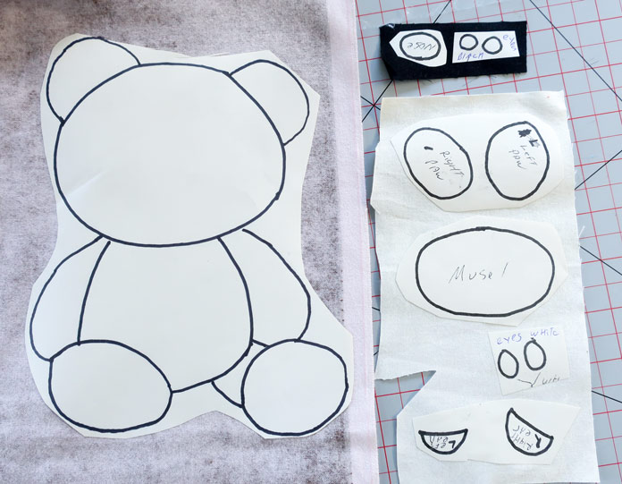 Teddy bear paper template pieces adhered to black and white fabric pieces; Odif 808 Spray and Fix Temporary Adhesive for Paper Patterns, Odif 606 Spray and Fix No-sew Fusible Adhesive Web, Odif 404 Spray and Fix Permanent Repositionable Adhesive for Craft Material, Odif 505 Temporary Quilt Basting Adhesive Fabric Spray