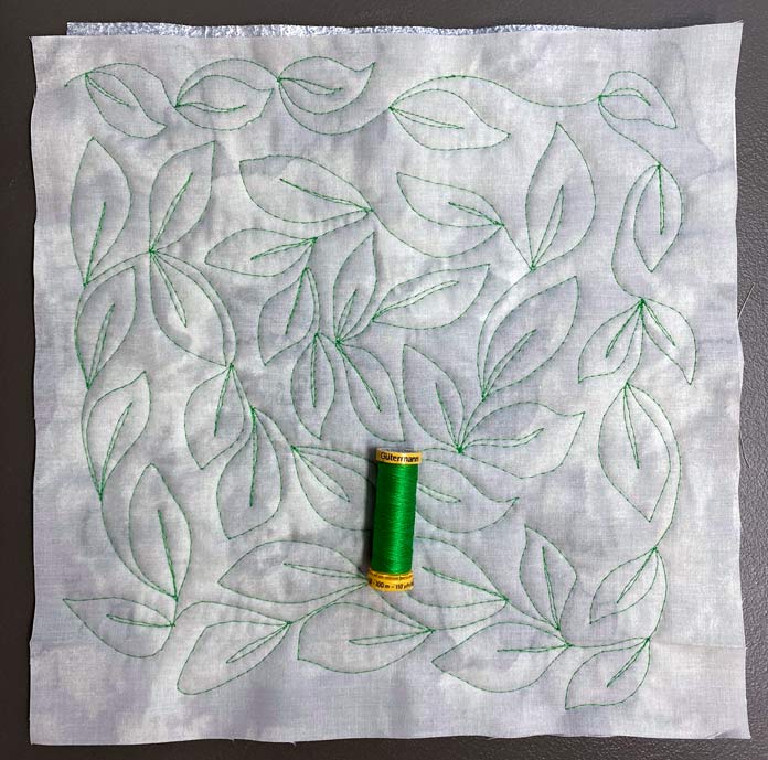 Continuous leaf free motion design on gray fabric with a spool of green thread on top; UNIQUE Quilting Therm Fleece, Fabric Creations Textured Grey fabric, Gütermann Thread, Gütermann Cotton Thread