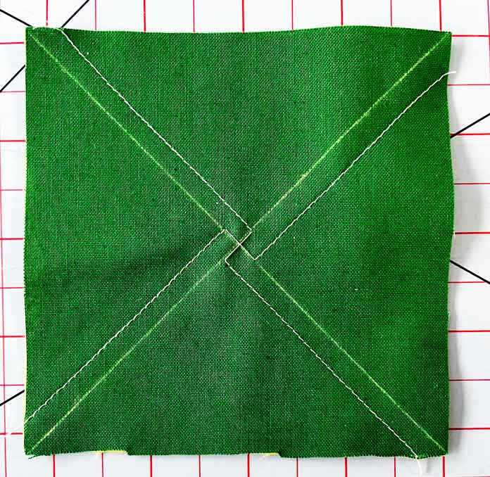 A second ¼” seam is sewn along the second diagonal line on a green fabric square. Clover Thread Cutter Pendant, Clover Chaco Liner, Clover Quilting Pins
