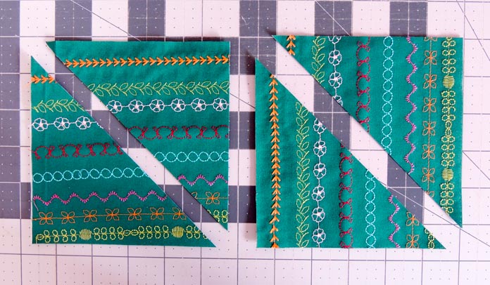 Two smaller squares of the green stitched background fabric cut once on the diagonal; laid out on a pink cutting mat.