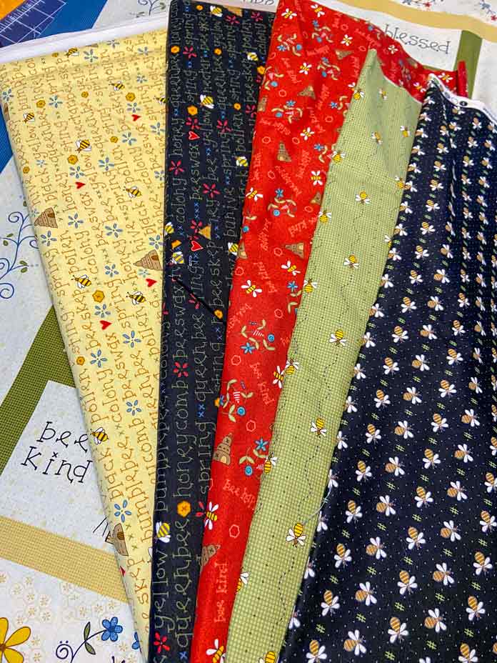 Cream, yellow, black, red and green fabrics printed with bees, bee skeps, flowers and words. 