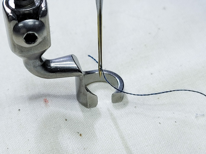 A metal foot on beige fabric with blue thread; PFAFF powerquilter 1600