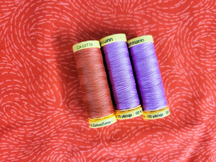 Two spools of pink and purple Gütermann Threads on an orange background; unboxing the Husqvarna VIKING ONXY 25