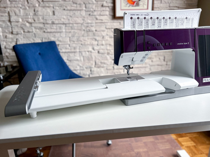 The PFAFF creative icon 2 Sewing and Embroidery Machine on the table with the embroidery unit in place and the lid open showing the stitch categories 