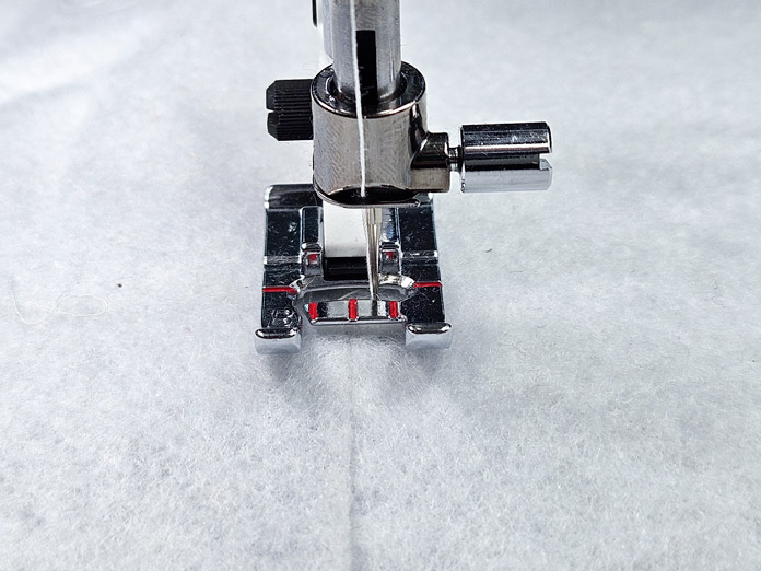 A metal presser foot joining two pieces of white fleece with a zigzag stitch